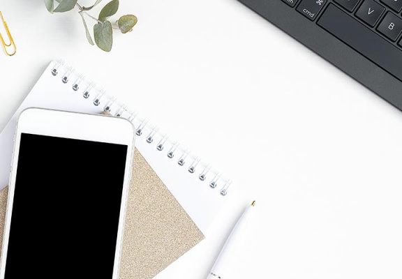 Clean white desk with black keyboard, and iphone laying on notebooks